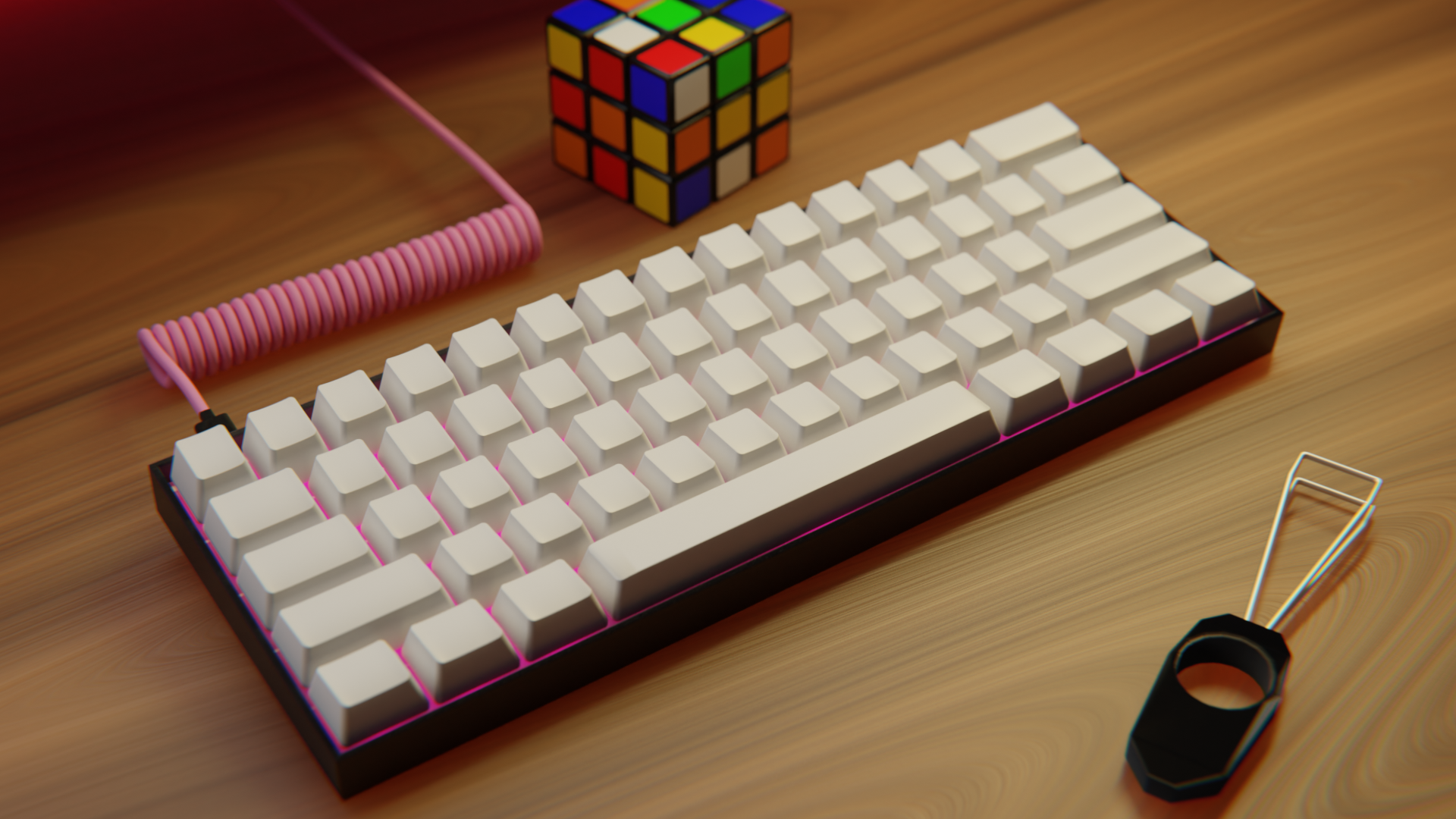Tastiera 60% con keycaps bianchi, scocca nera e led rosa. Dietro la tastiera un cubo di Rubik non risolto e davanti la tastiera un keycaps puller. I keycaps sono vuoti. Il cavo della tastiera è a spirale ed è rosa. Il tavolo della scrivania è di legno